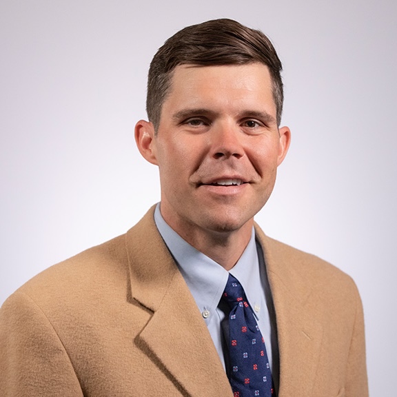 Brandon is smiling and appears to be in a professional setting, wearing a button-up shirt and jacket.